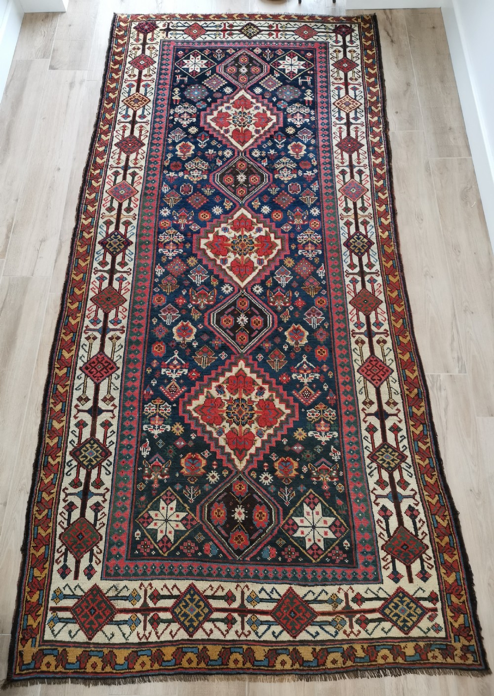 A hand-knotted Persian Veramin wool runner rug featuring diamond-shaped central medallions in crimson red, navy blue, and ivory set within a geometric border.