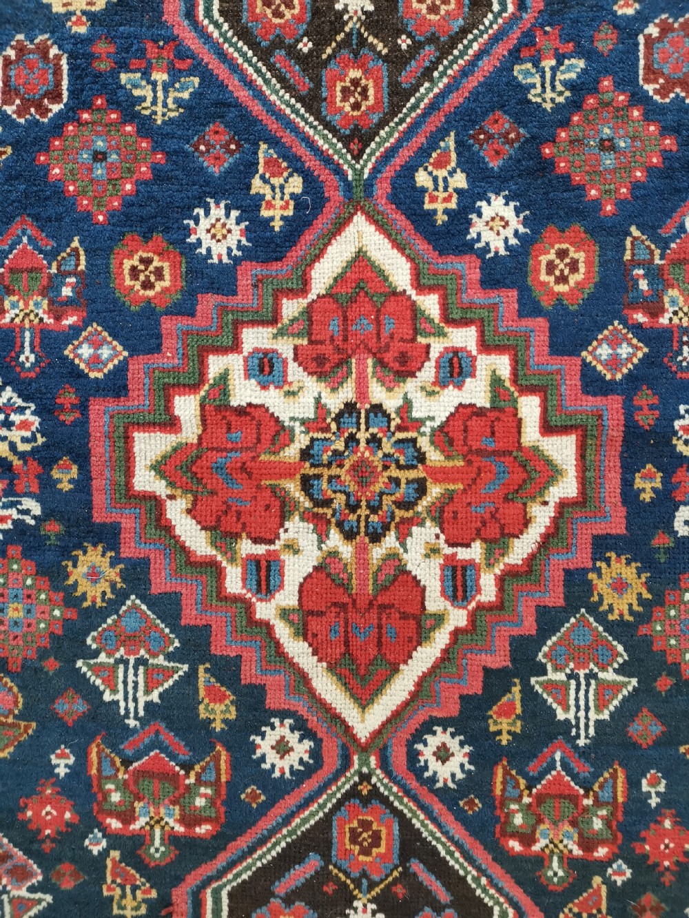 A hand-knotted Persian Veramin wool runner rug featuring diamond-shaped central medallions in crimson red, navy blue, and ivory set within a geometric border. View V