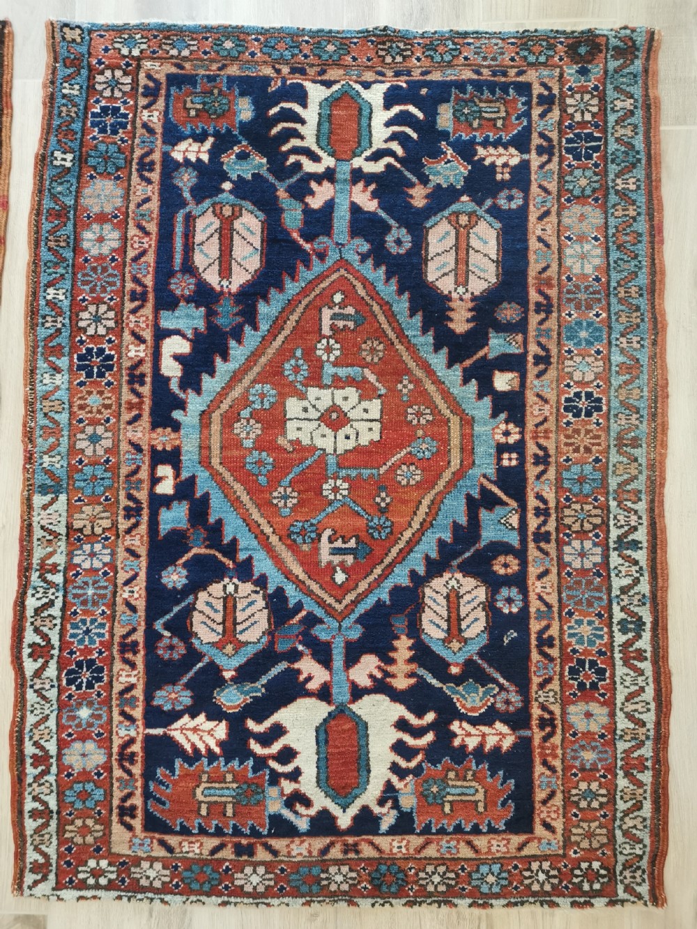 A hand-knotted antique Karaja wool rug featuring a navy field decorated with a central red geometric diamond medallion and colourful tribal motifs within a geometric border.