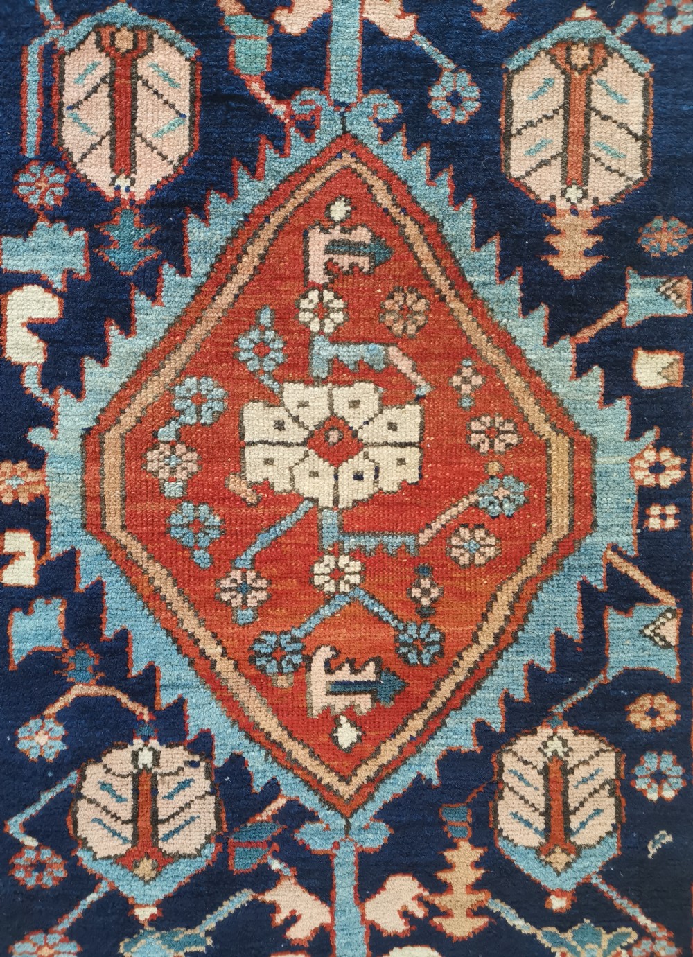 A hand-knotted antique Karaja wool rug featuring a navy field decorated with a central red geometric diamond medallion and colourful tribal motifs within a geometric border. View IV