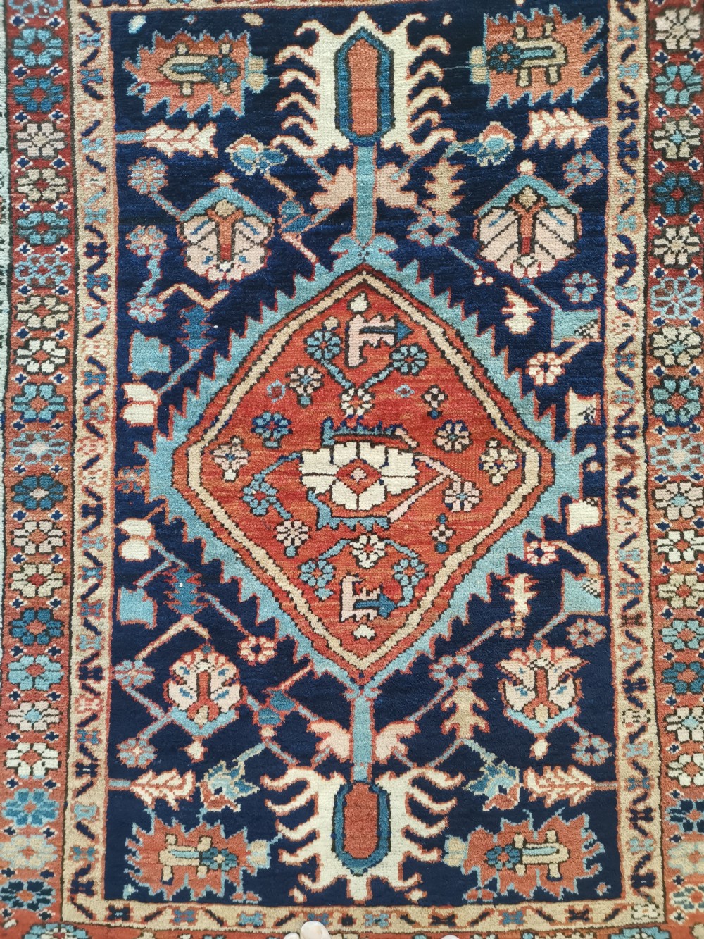 A hand-knotted antique Karaja wool rug featuring a navy field decorated with a central red geometric diamond medallion and colourful tribal motifs within a geometric border. View V