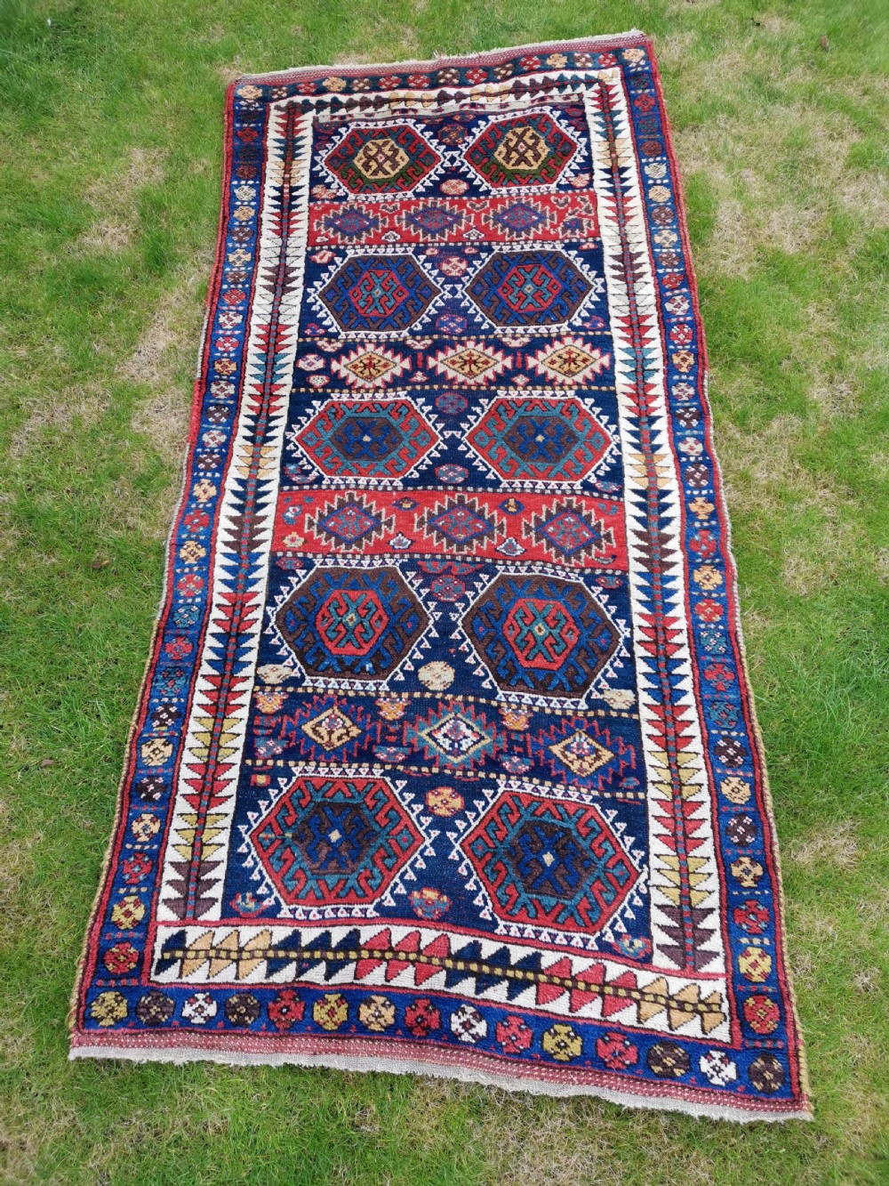 A hand-knotted tribal Jaf Kurdish wool rug featuring geometric hexagonal hooked motifs in deep navy blue, red, ochre, and cream.
