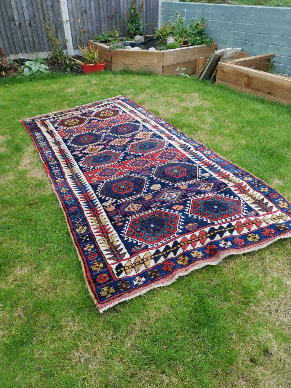 A hand-knotted tribal Jaf Kurdish wool rug featuring geometric hexagonal hooked motifs in deep navy blue, red, ochre, and cream. View IV