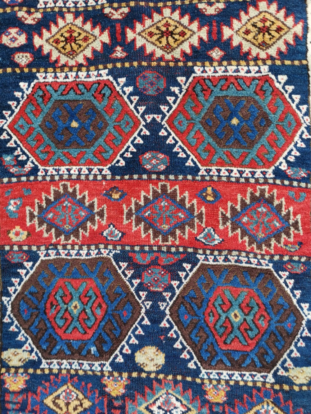 A hand-knotted tribal Jaf Kurdish wool rug featuring geometric hexagonal hooked motifs in deep navy blue, red, ochre, and cream. View V