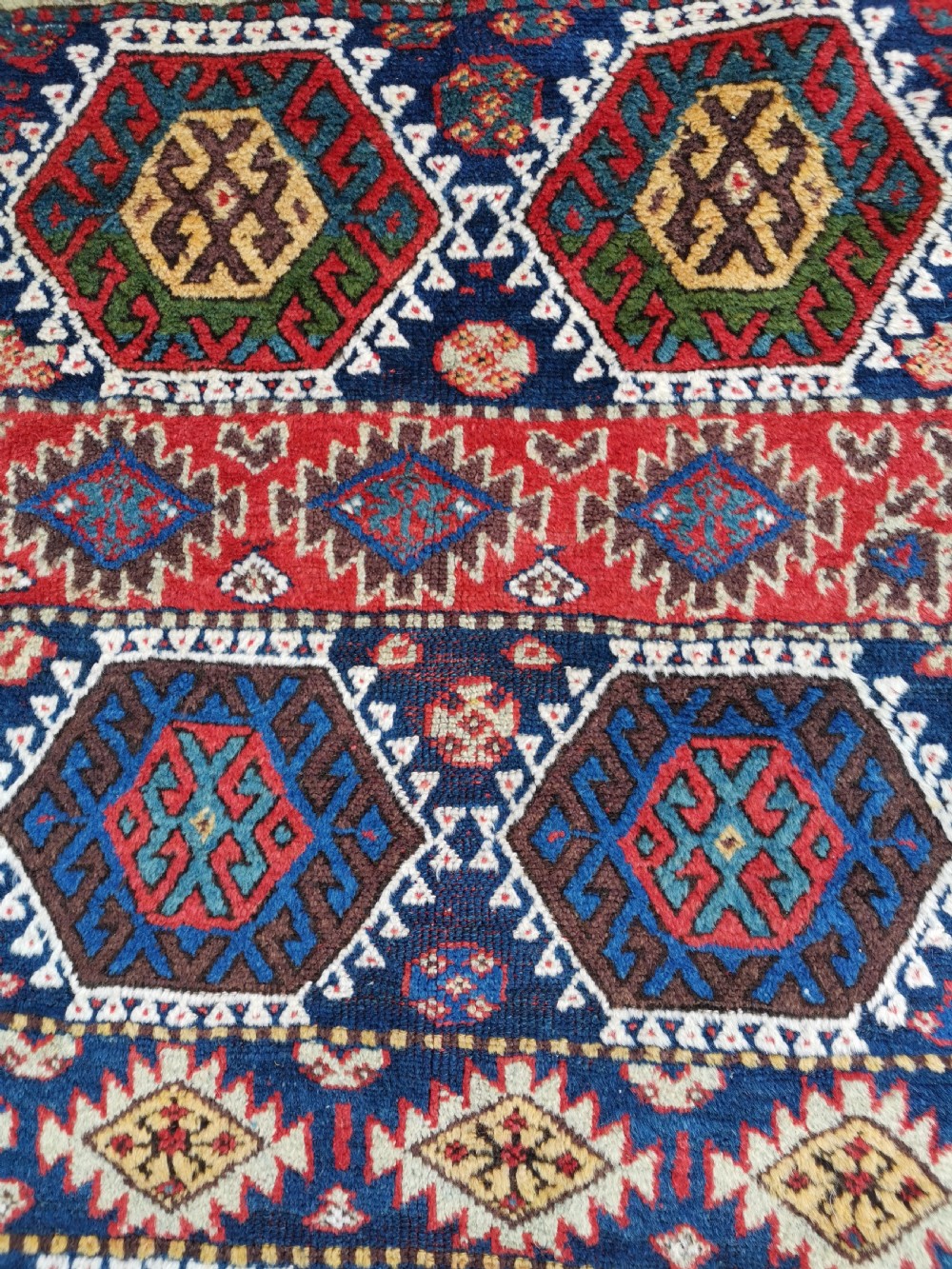 A hand-knotted tribal Jaf Kurdish wool rug featuring geometric hexagonal hooked motifs in deep navy blue, red, ochre, and cream. View VI
