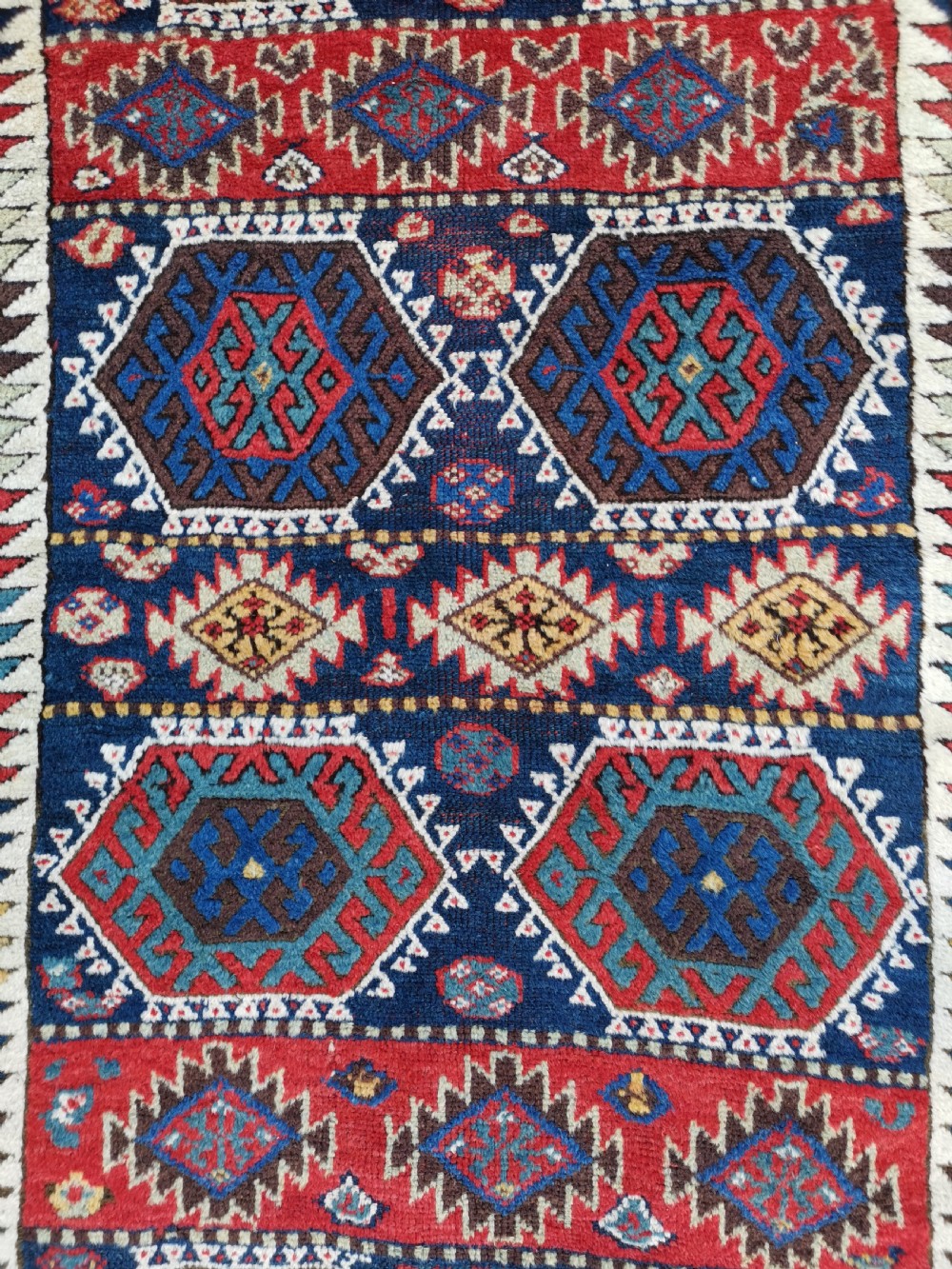 A hand-knotted tribal Jaf Kurdish wool rug featuring geometric hexagonal hooked motifs in deep navy blue, red, ochre, and cream. View VII