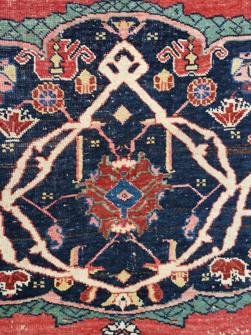 An antique hand-knotted Persian Bijar wool rug featuring a red central field, dark navy medallion, and geometric floral borders. View IV