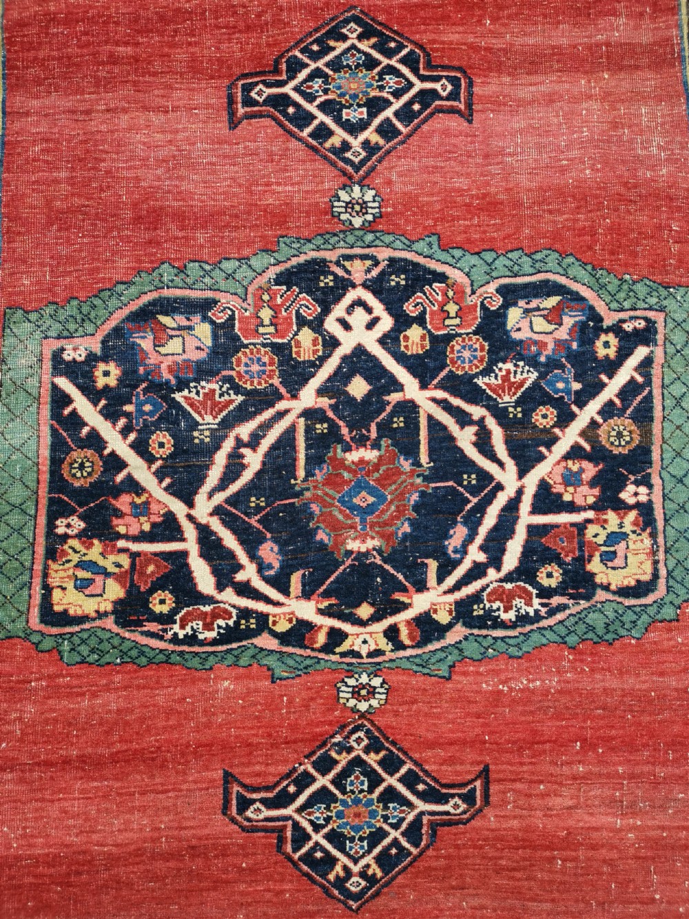 An antique hand-knotted Persian Bijar wool rug featuring a red central field, dark navy medallion, and geometric floral borders. View V
