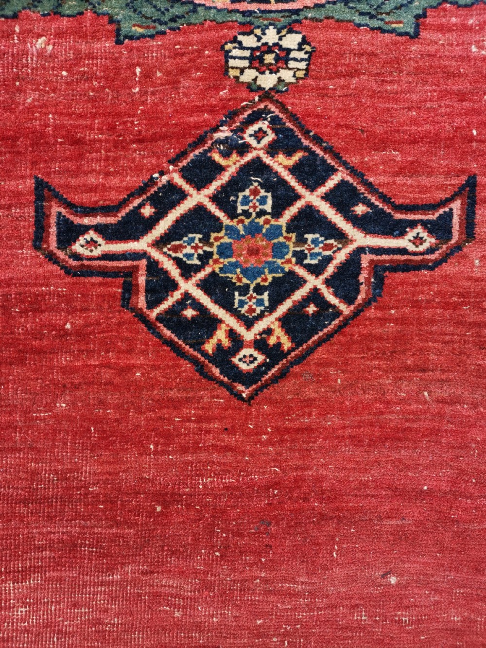 An antique hand-knotted Persian Bijar wool rug featuring a red central field, dark navy medallion, and geometric floral borders. View VI