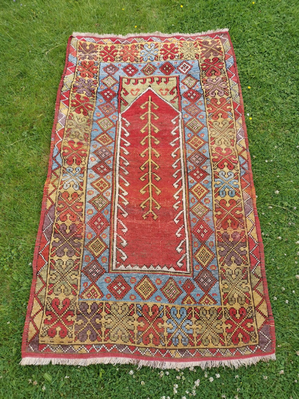 A hand-knotted antique Anatolian Konya prayer rug featuring a red mihrab arch motif, central tree pattern, and geometric multi-coloured borders.