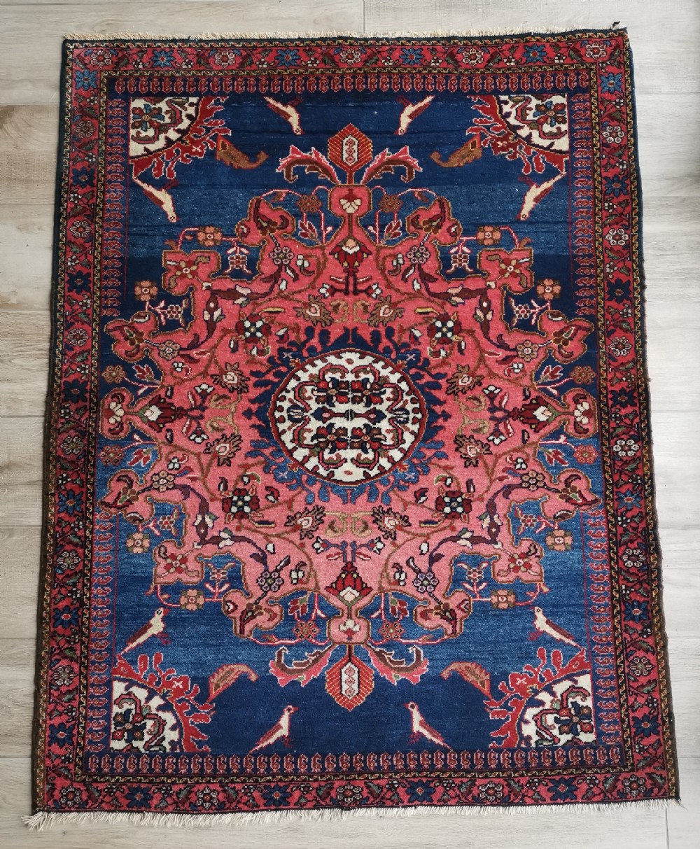 A hand-knotted antique Persian Tafresh wool rug featuring a deep navy blue field, a prominent rose pink central medallion, ornate floral spandrels, and bird motifs.
