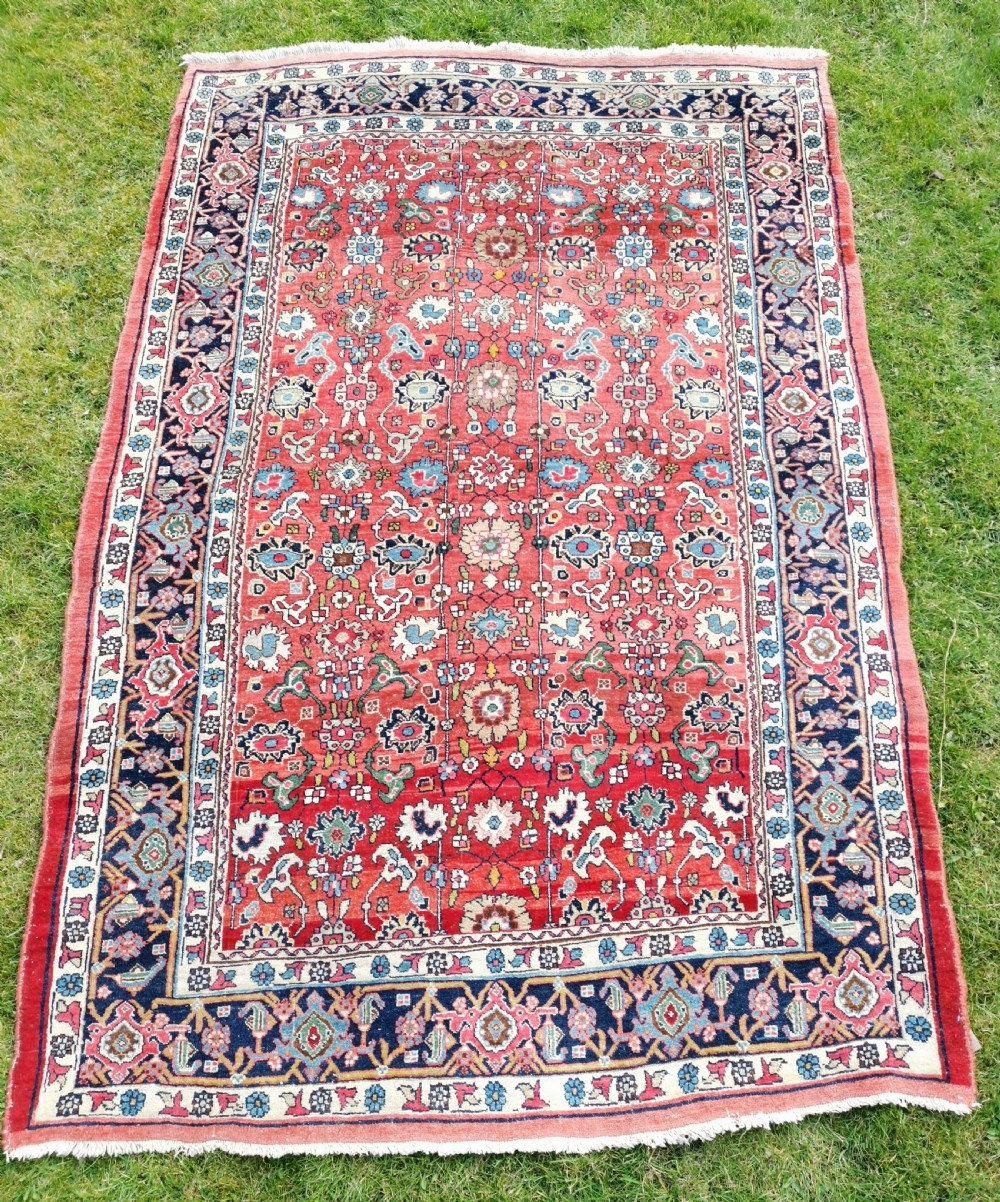 A rectangular hand-knotted Persian Bijar rug displaying a dense floral pattern across a red field bordered by navy blue decorative banding.