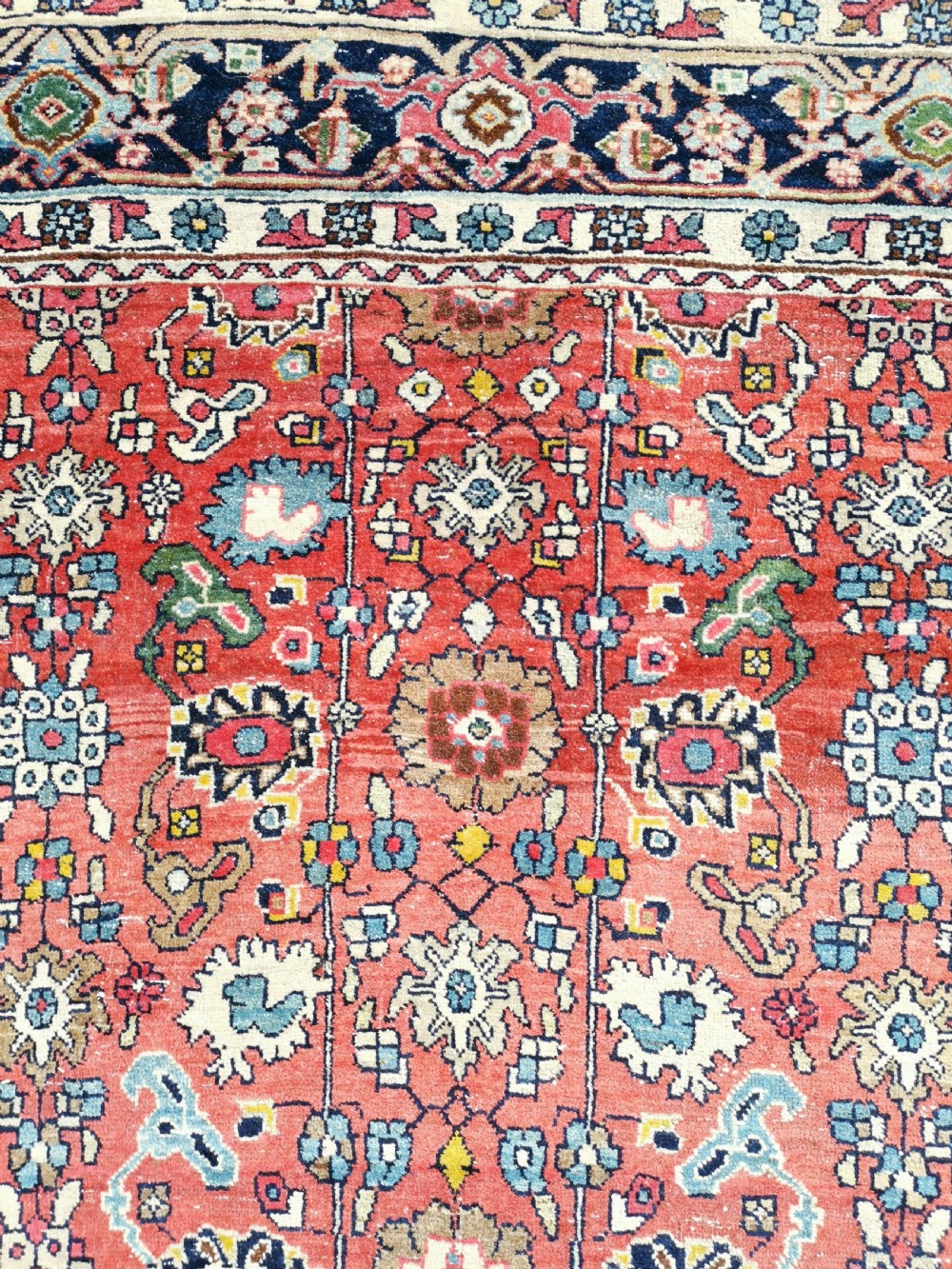 A rectangular hand-knotted Persian Bijar rug displaying a dense floral pattern across a red field bordered by navy blue decorative banding. View III