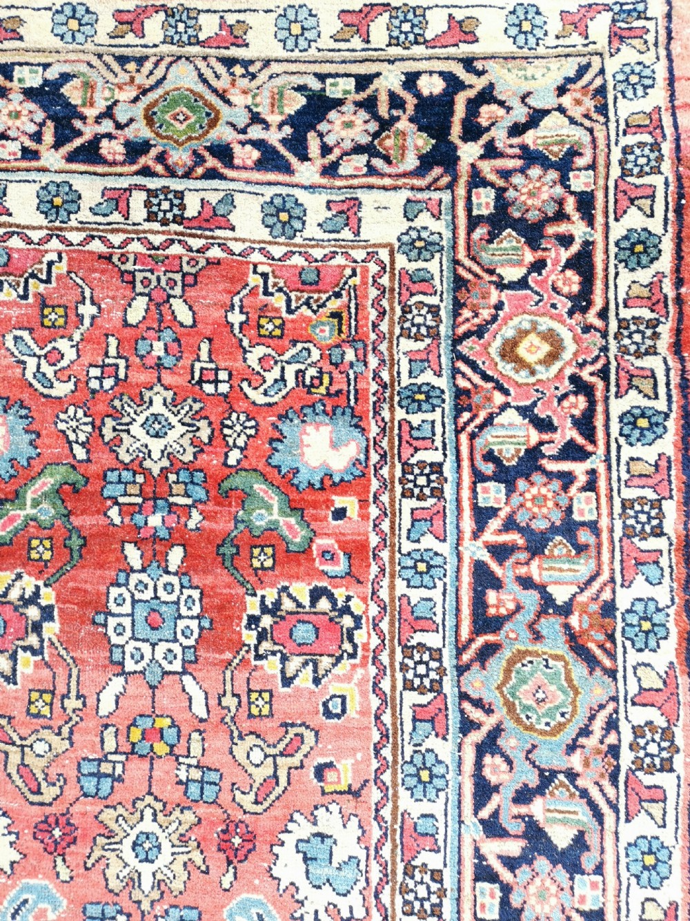 A rectangular hand-knotted Persian Bijar rug displaying a dense floral pattern across a red field bordered by navy blue decorative banding. View IV