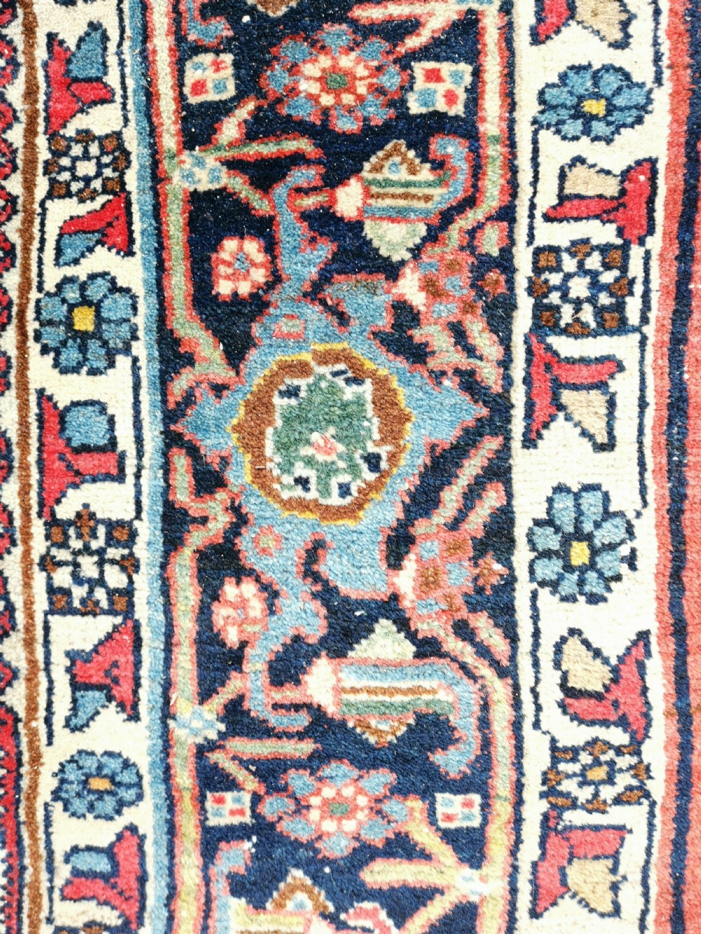 A rectangular hand-knotted Persian Bijar rug displaying a dense floral pattern across a red field bordered by navy blue decorative banding. View V