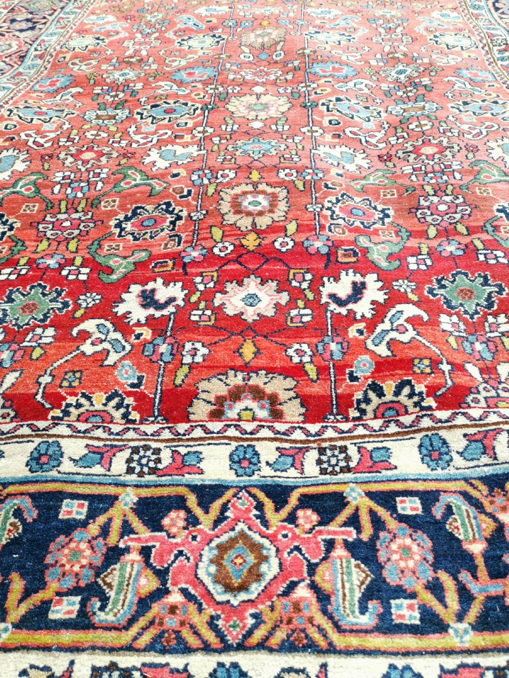 A rectangular hand-knotted Persian Bijar rug displaying a dense floral pattern across a red field bordered by navy blue decorative banding. View VII