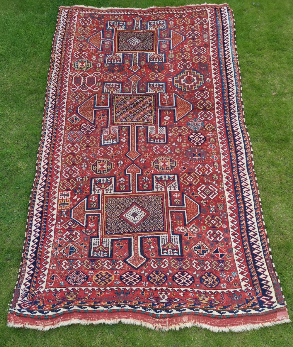 A handwoven rectangular Quchan Kurdish wool rug featuring geometric stepped medallions and repeating motifs in shades of terracotta red, navy blue, and cream.