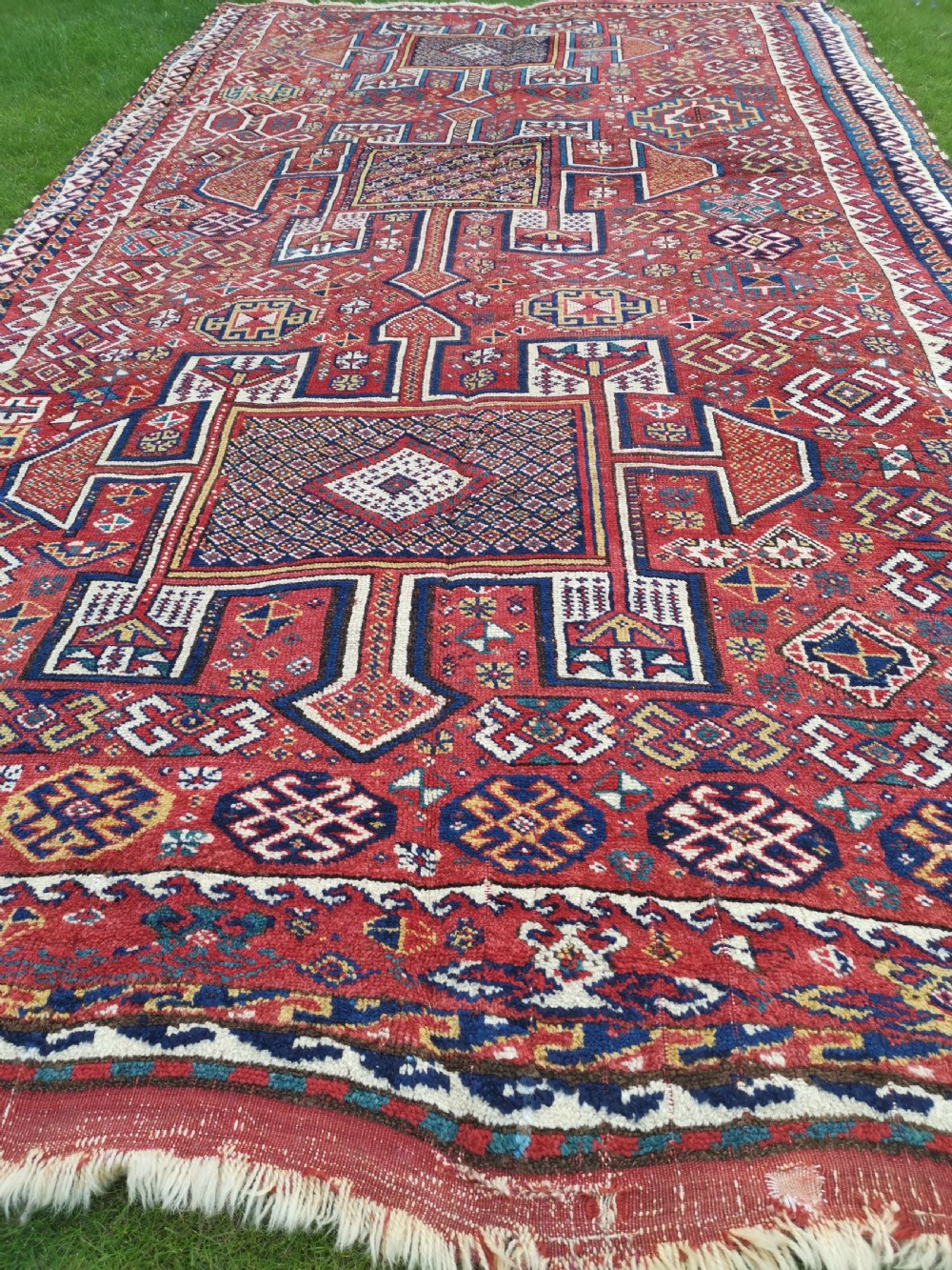 A handwoven rectangular Quchan Kurdish wool rug featuring geometric stepped medallions and repeating motifs in shades of terracotta red, navy blue, and cream. View II
