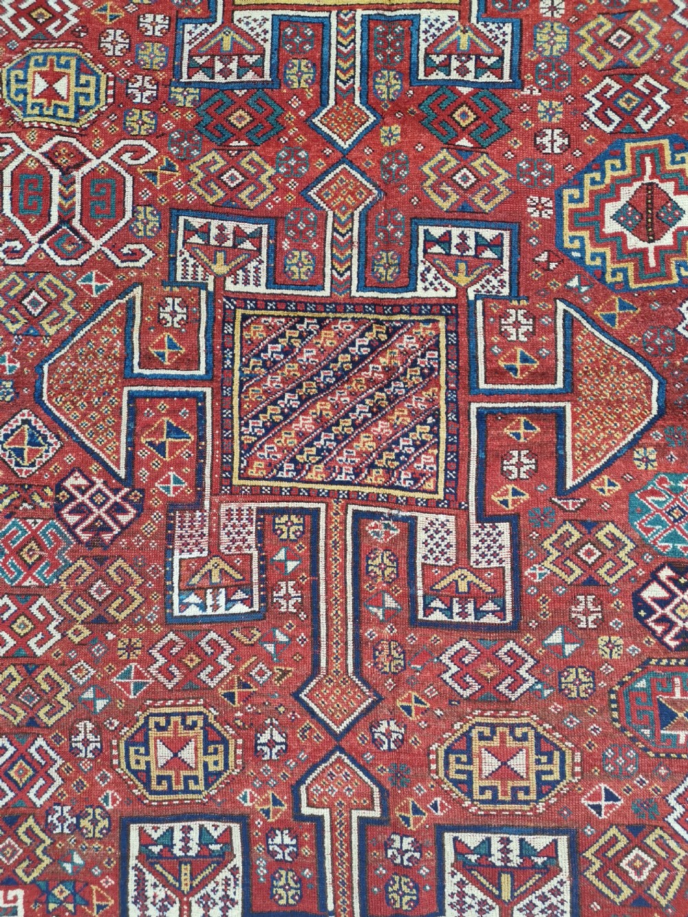 A handwoven rectangular Quchan Kurdish wool rug featuring geometric stepped medallions and repeating motifs in shades of terracotta red, navy blue, and cream. View III