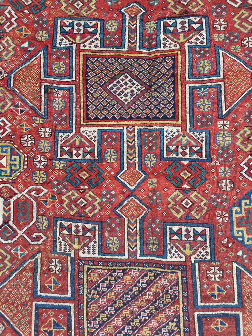 A handwoven rectangular Quchan Kurdish wool rug featuring geometric stepped medallions and repeating motifs in shades of terracotta red, navy blue, and cream. View IV