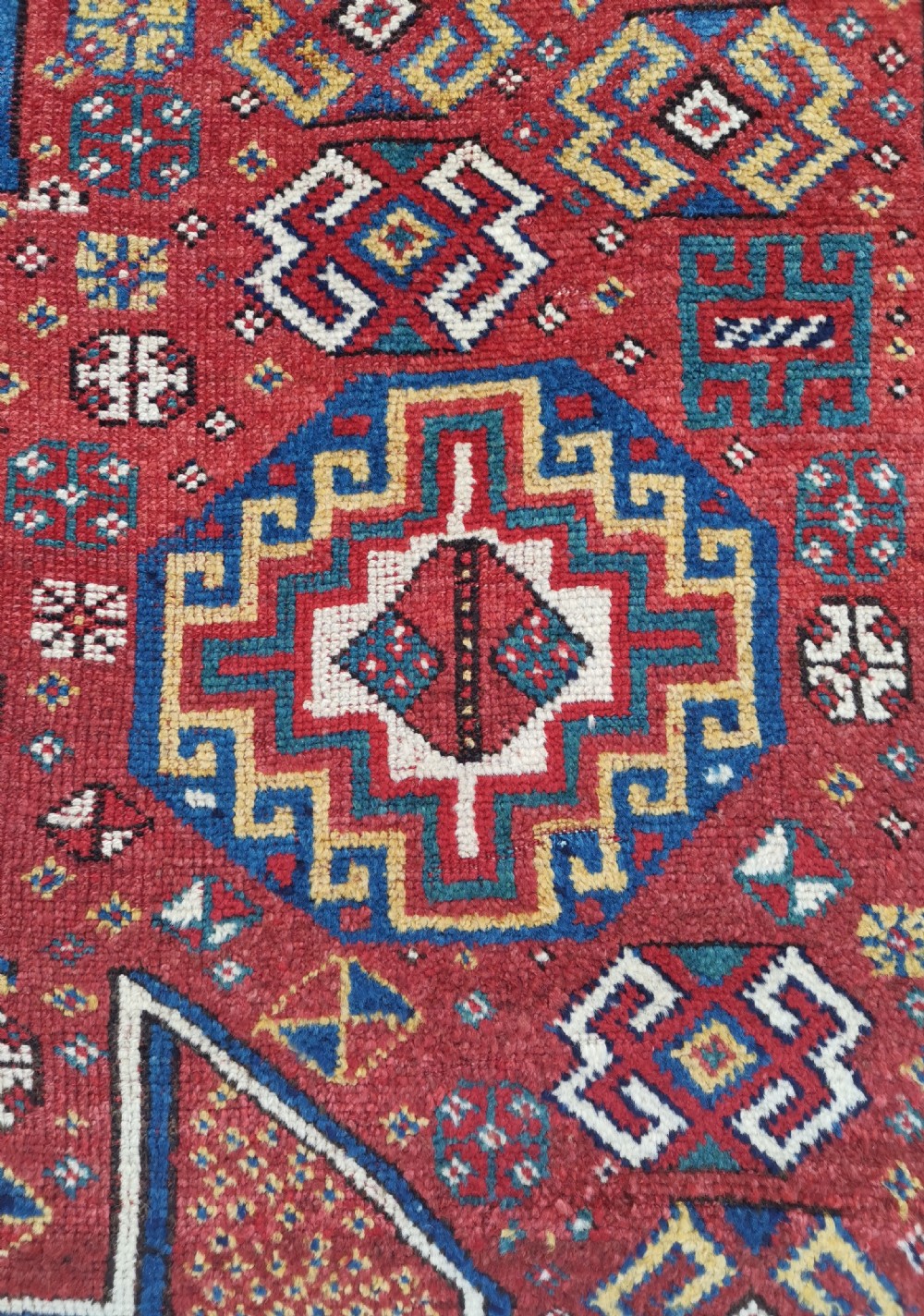 A handwoven rectangular Quchan Kurdish wool rug featuring geometric stepped medallions and repeating motifs in shades of terracotta red, navy blue, and cream. View VI