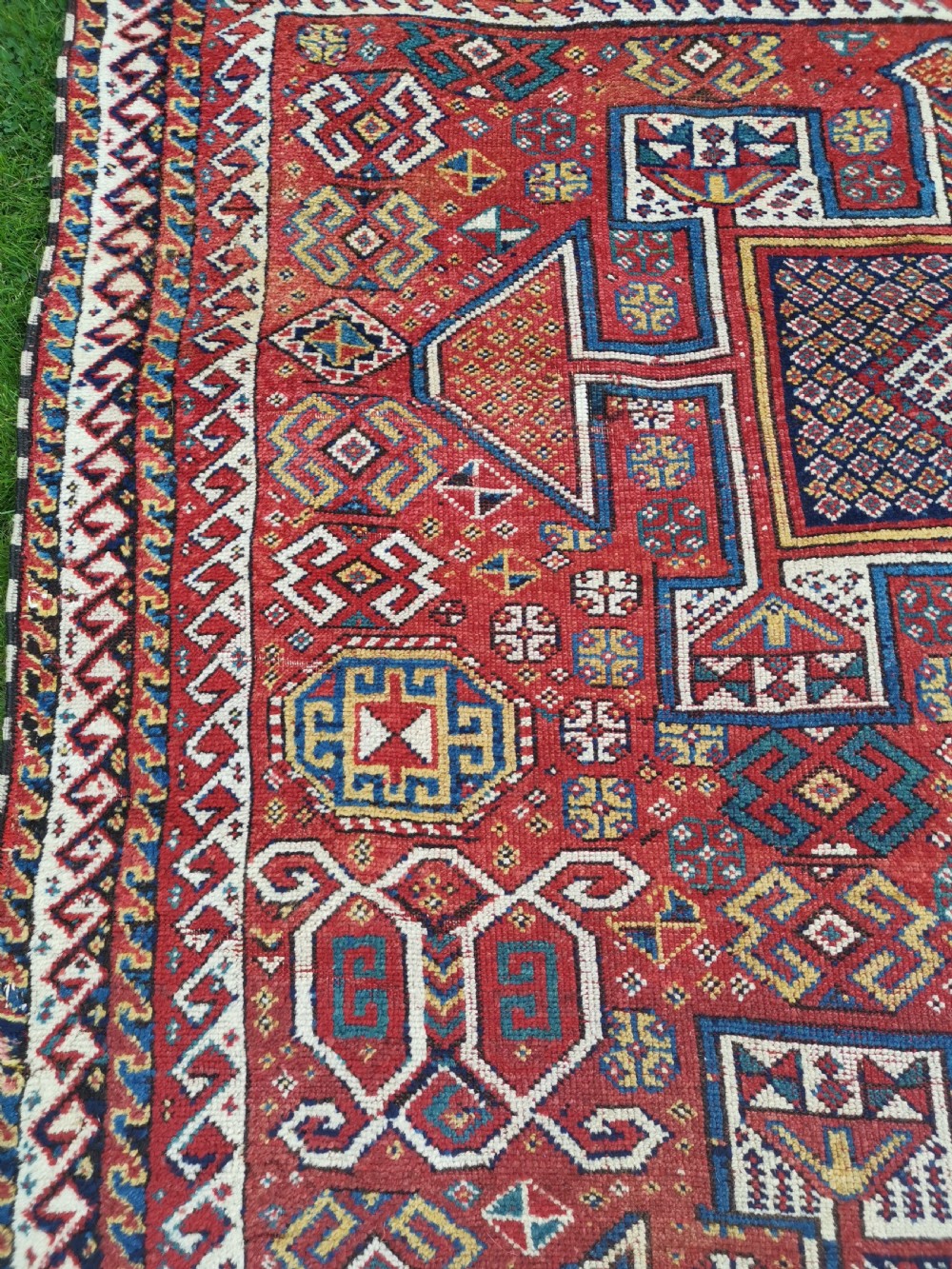 A handwoven rectangular Quchan Kurdish wool rug featuring geometric stepped medallions and repeating motifs in shades of terracotta red, navy blue, and cream. View VII