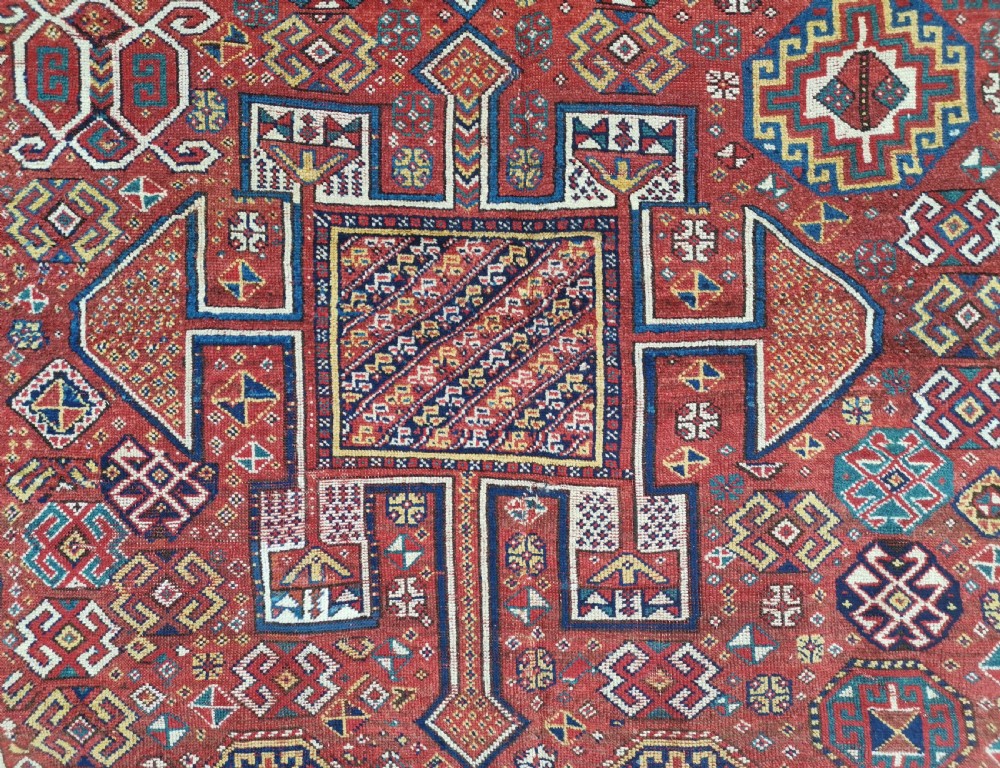 A handwoven rectangular Quchan Kurdish wool rug featuring geometric stepped medallions and repeating motifs in shades of terracotta red, navy blue, and cream. View IX