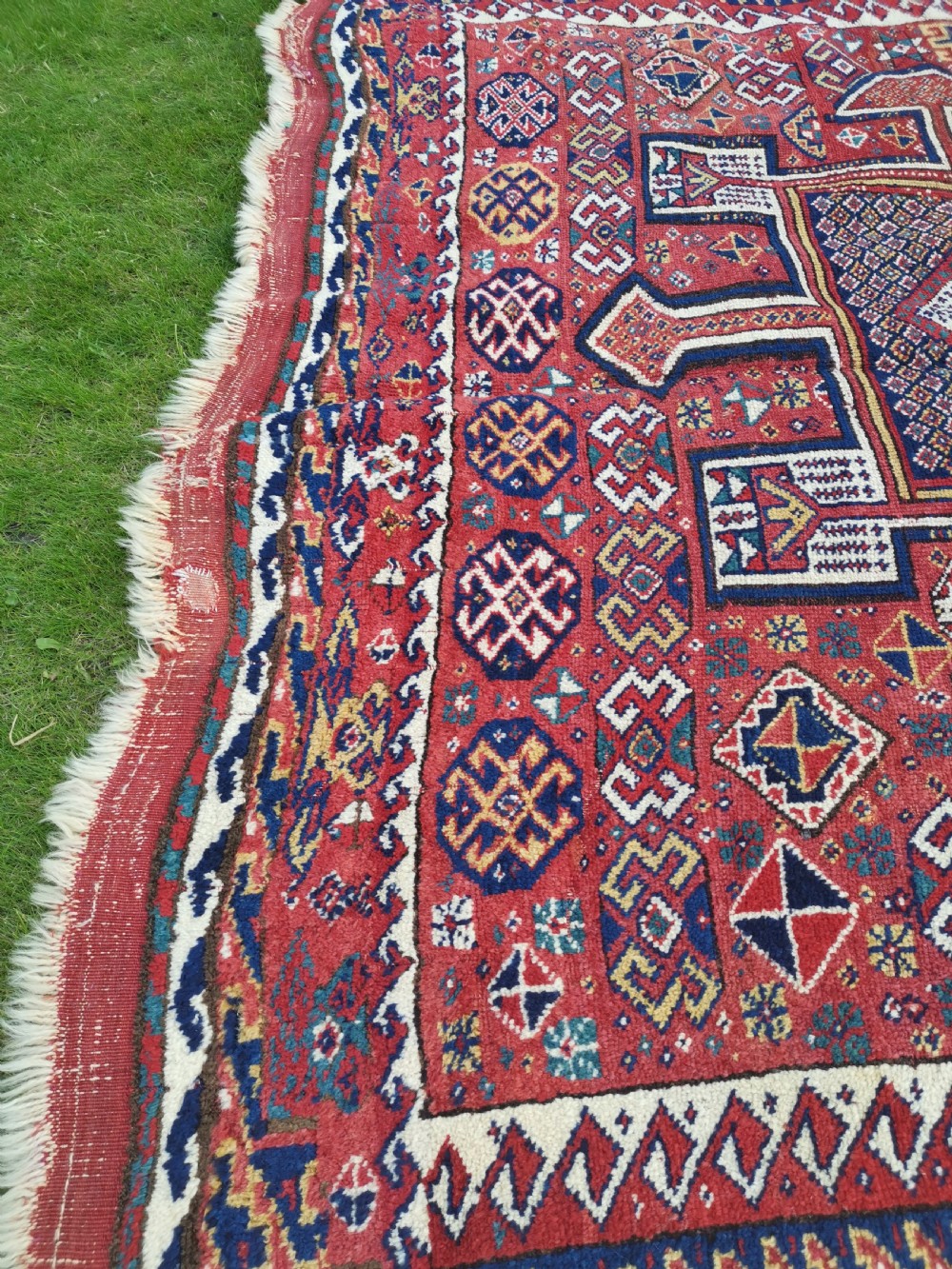 A handwoven rectangular Quchan Kurdish wool rug featuring geometric stepped medallions and repeating motifs in shades of terracotta red, navy blue, and cream. View XII