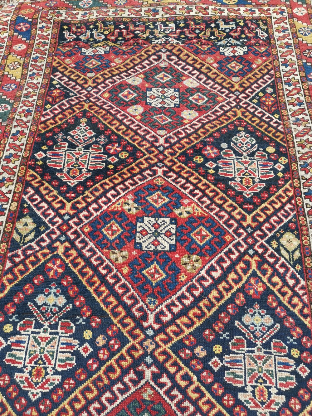 An antique Persian Luri hand-knotted wool runner featuring central diamond medallions in red and navy blue framed by geometric borders. View III