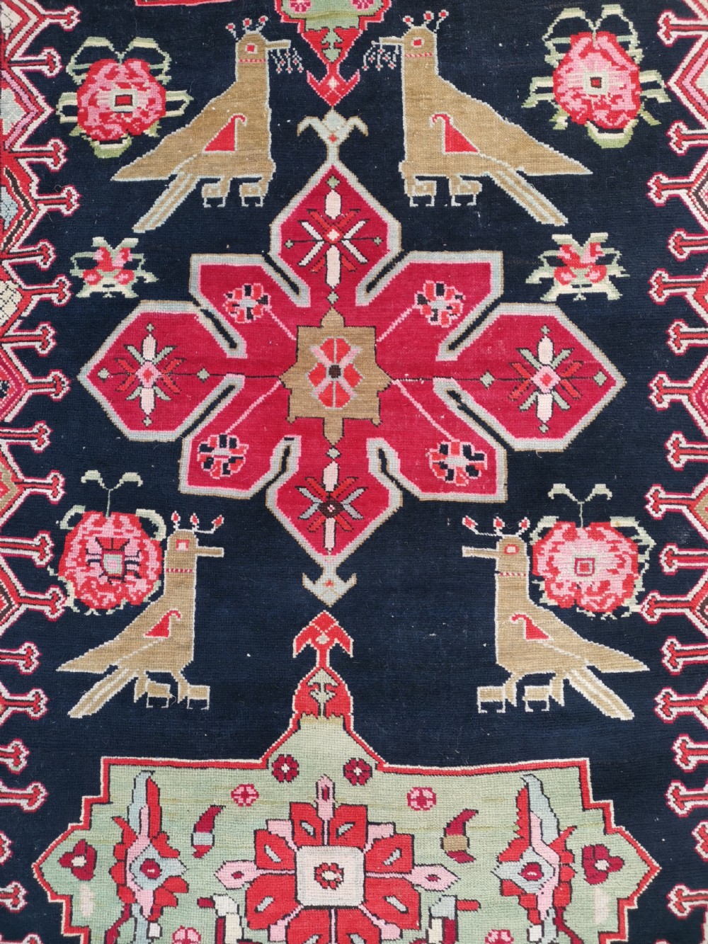A detailed close-up view of an antique dark navy hand-knotted wool rug featuring stylized bird figures, red geometric star medallions, and floral motifs.