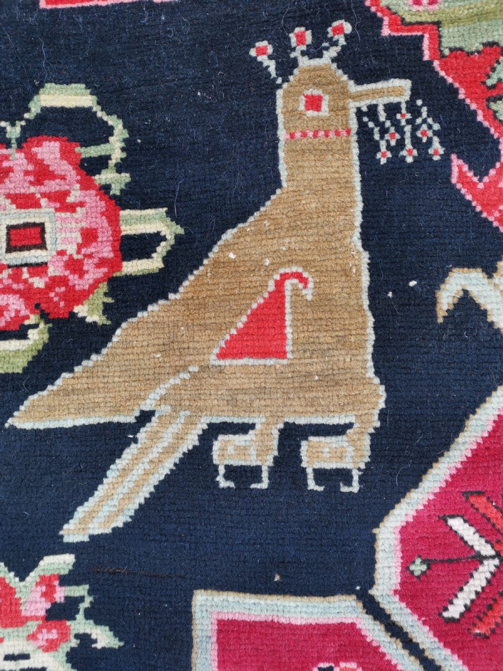 A detailed close-up view of an antique dark navy hand-knotted wool rug featuring stylized bird figures, red geometric star medallions, and floral motifs. View VII