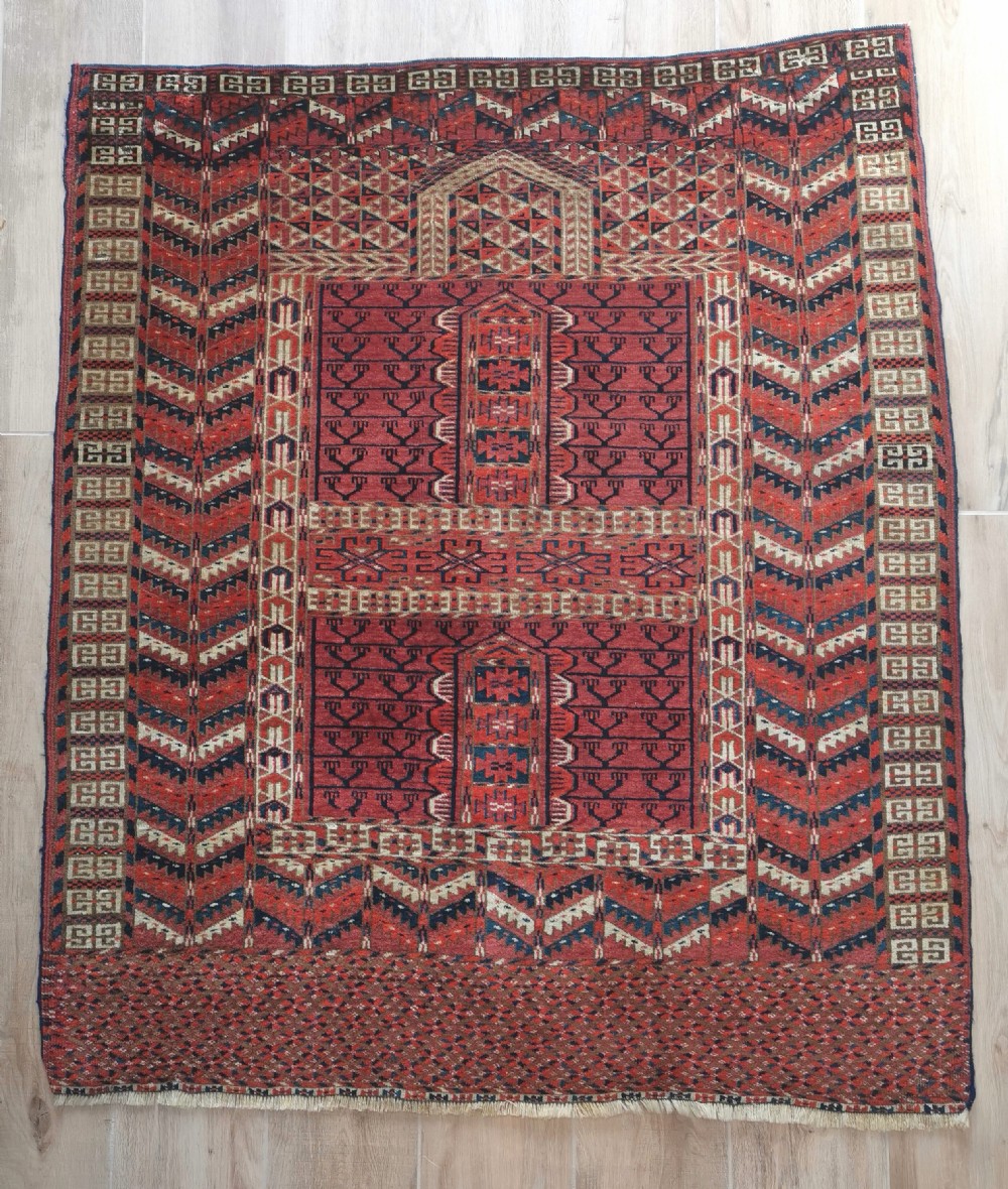 An antique hand-knotted Tekke Turkmen engsi wool rug featuring a red four-panel hatchli design with geometric tribal borders.