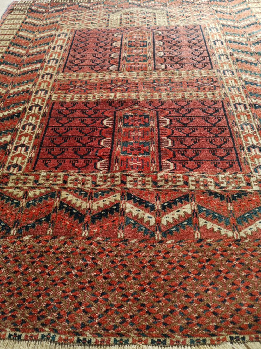 An antique hand-knotted Tekke Turkmen engsi wool rug featuring a red four-panel hatchli design with geometric tribal borders. View IV