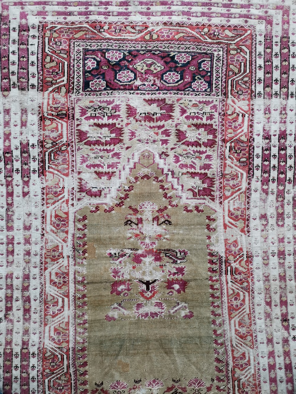 An antique Anatolian Ghiordes prayer rug featuring a central beige arched mihrab panel framed by multiple geometric borders in crimson red and cream wool. View II