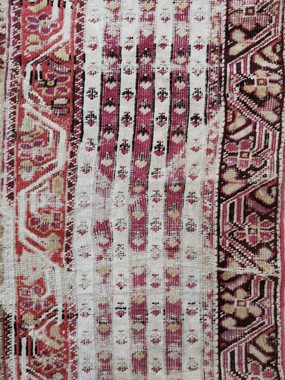 An antique Anatolian Ghiordes prayer rug featuring a central beige arched mihrab panel framed by multiple geometric borders in crimson red and cream wool. View III