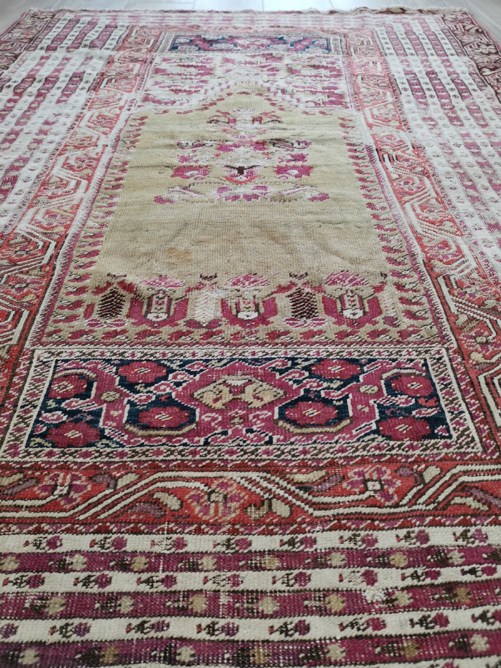 An antique Anatolian Ghiordes prayer rug featuring a central beige arched mihrab panel framed by multiple geometric borders in crimson red and cream wool. View IV