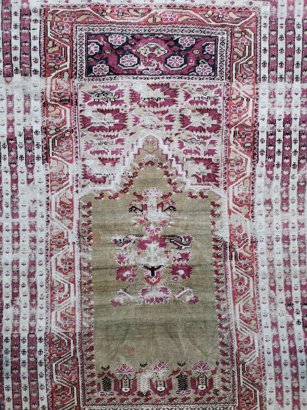 An antique Anatolian Ghiordes prayer rug featuring a central beige arched mihrab panel framed by multiple geometric borders in crimson red and cream wool. View V