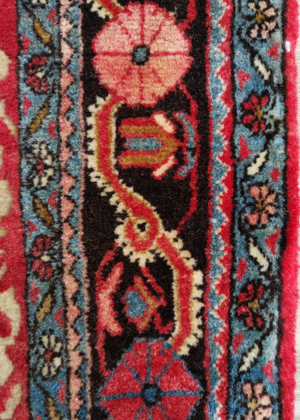 A hand-knotted rectangular antique Sarouk wool rug featuring a crimson red repeating floral pattern on a cream ground framed by a dark floral border. View III