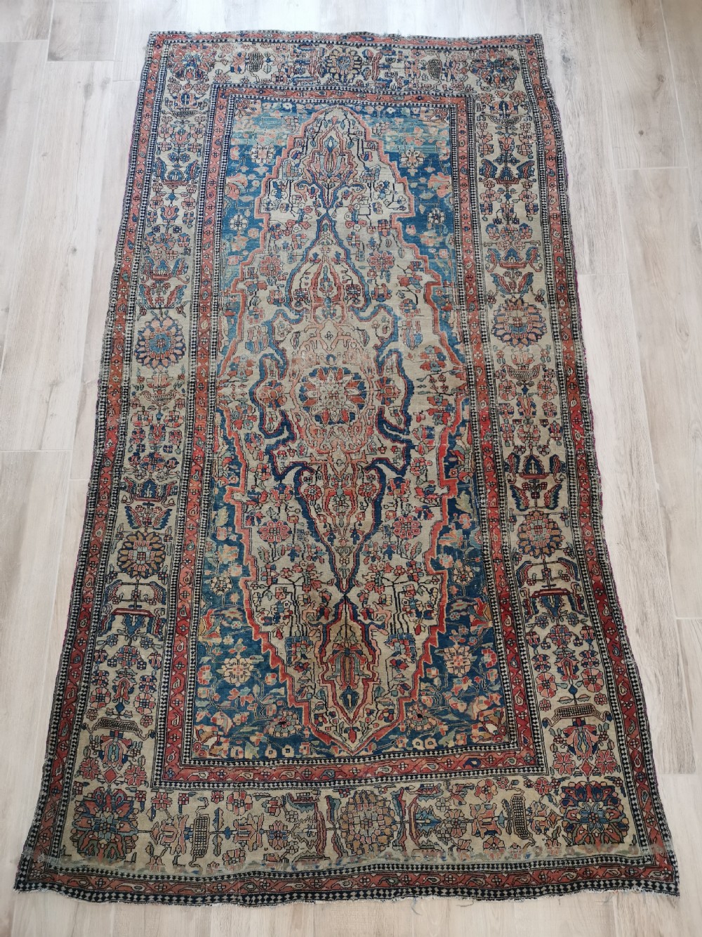 An antique hand-knotted Kashan Persian rug featuring a central blue medallion on a cream field with detailed floral borders.