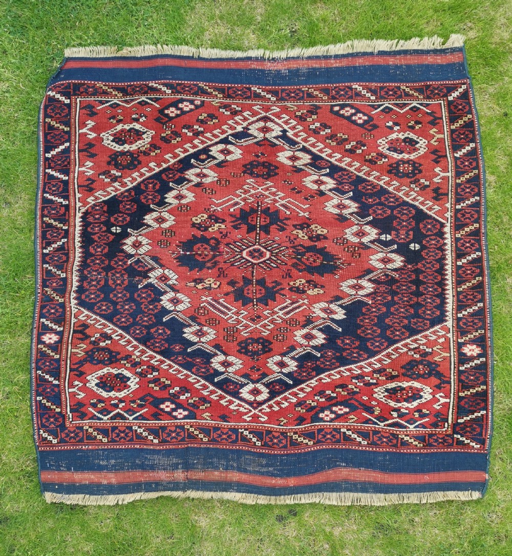 An antique square Anatolian Bergama wool rug featuring a central diamond medallion and geometric motifs in red, navy blue, and cream.