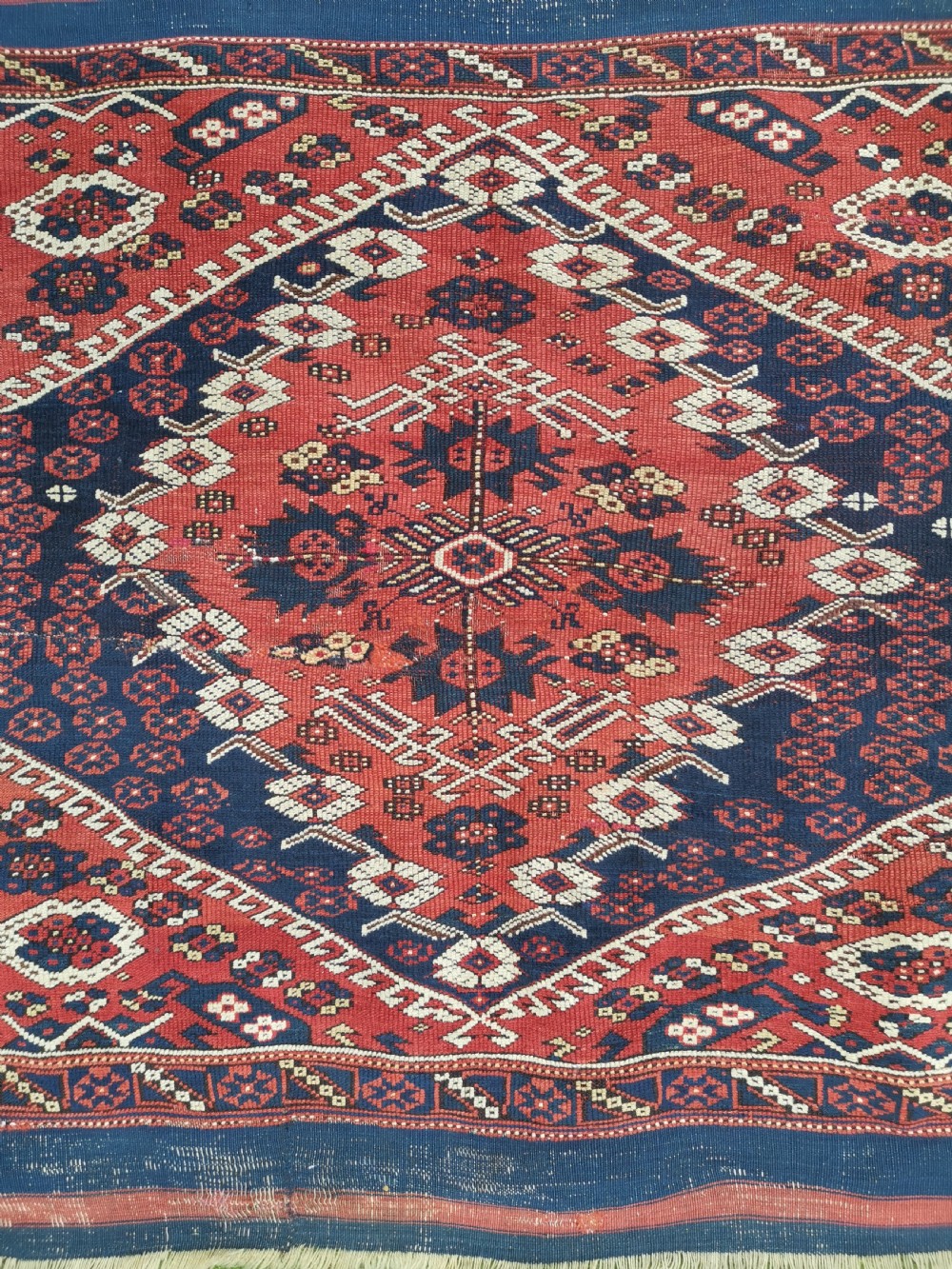 An antique square Anatolian Bergama wool rug featuring a central diamond medallion and geometric motifs in red, navy blue, and cream. View II