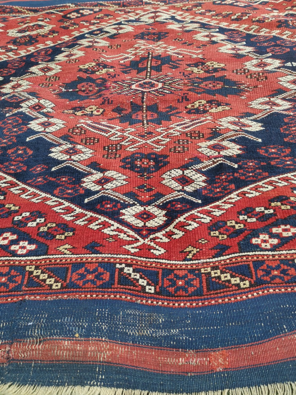 An antique square Anatolian Bergama wool rug featuring a central diamond medallion and geometric motifs in red, navy blue, and cream. View IV