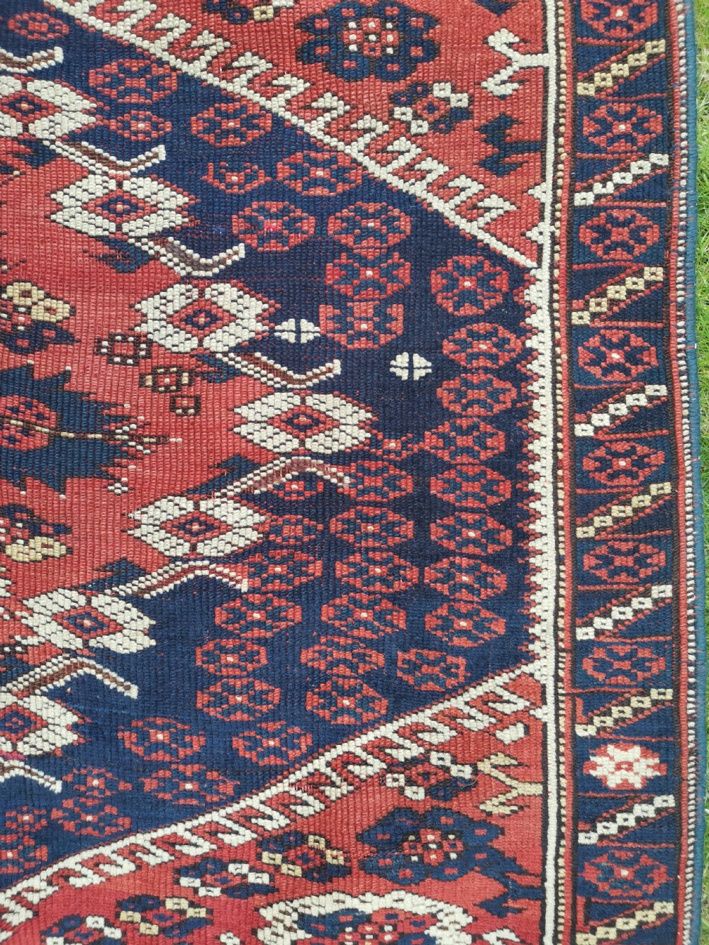 An antique square Anatolian Bergama wool rug featuring a central diamond medallion and geometric motifs in red, navy blue, and cream. View VI