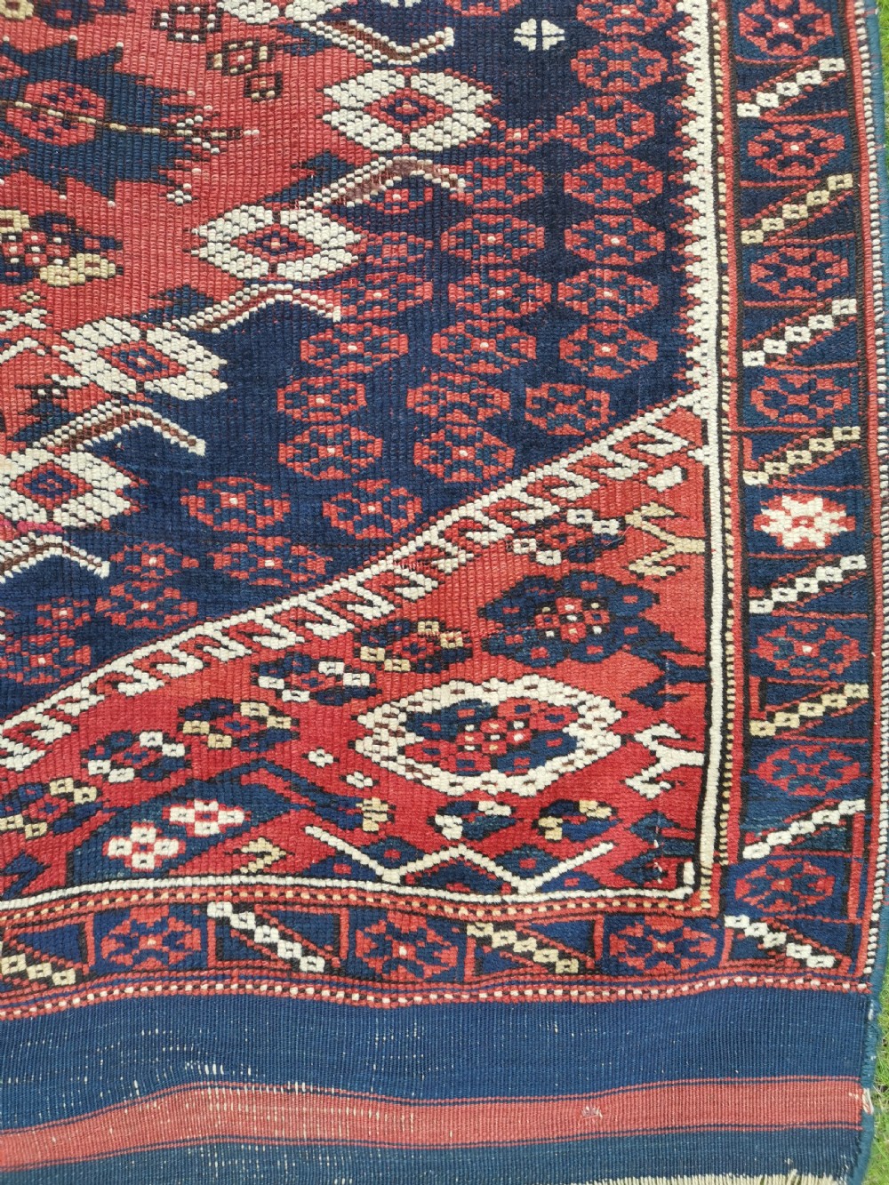 An antique square Anatolian Bergama wool rug featuring a central diamond medallion and geometric motifs in red, navy blue, and cream. View VII