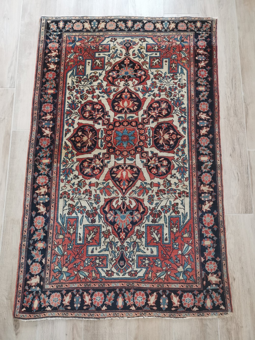 A rectangular hand-knotted antique Persian Sarouk rug featuring a central floral medallion on an ivory field with a navy floral border.