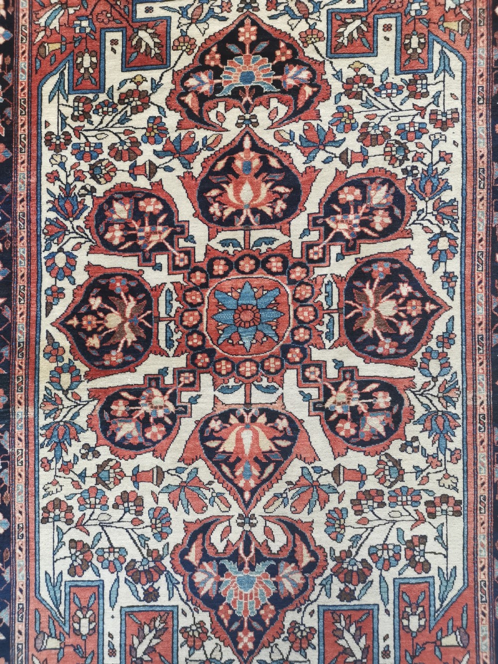 A rectangular hand-knotted antique Persian Sarouk rug featuring a central floral medallion on an ivory field with a navy floral border. View II