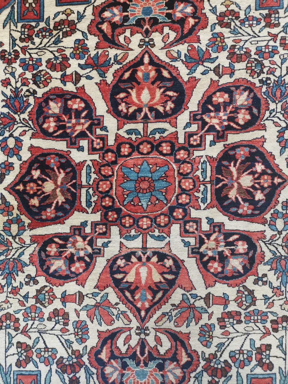 A rectangular hand-knotted antique Persian Sarouk rug featuring a central floral medallion on an ivory field with a navy floral border. View III