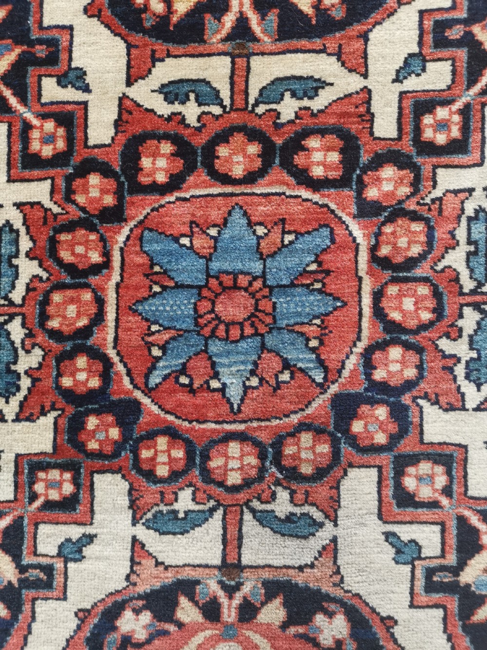 A rectangular hand-knotted antique Persian Sarouk rug featuring a central floral medallion on an ivory field with a navy floral border. View IV