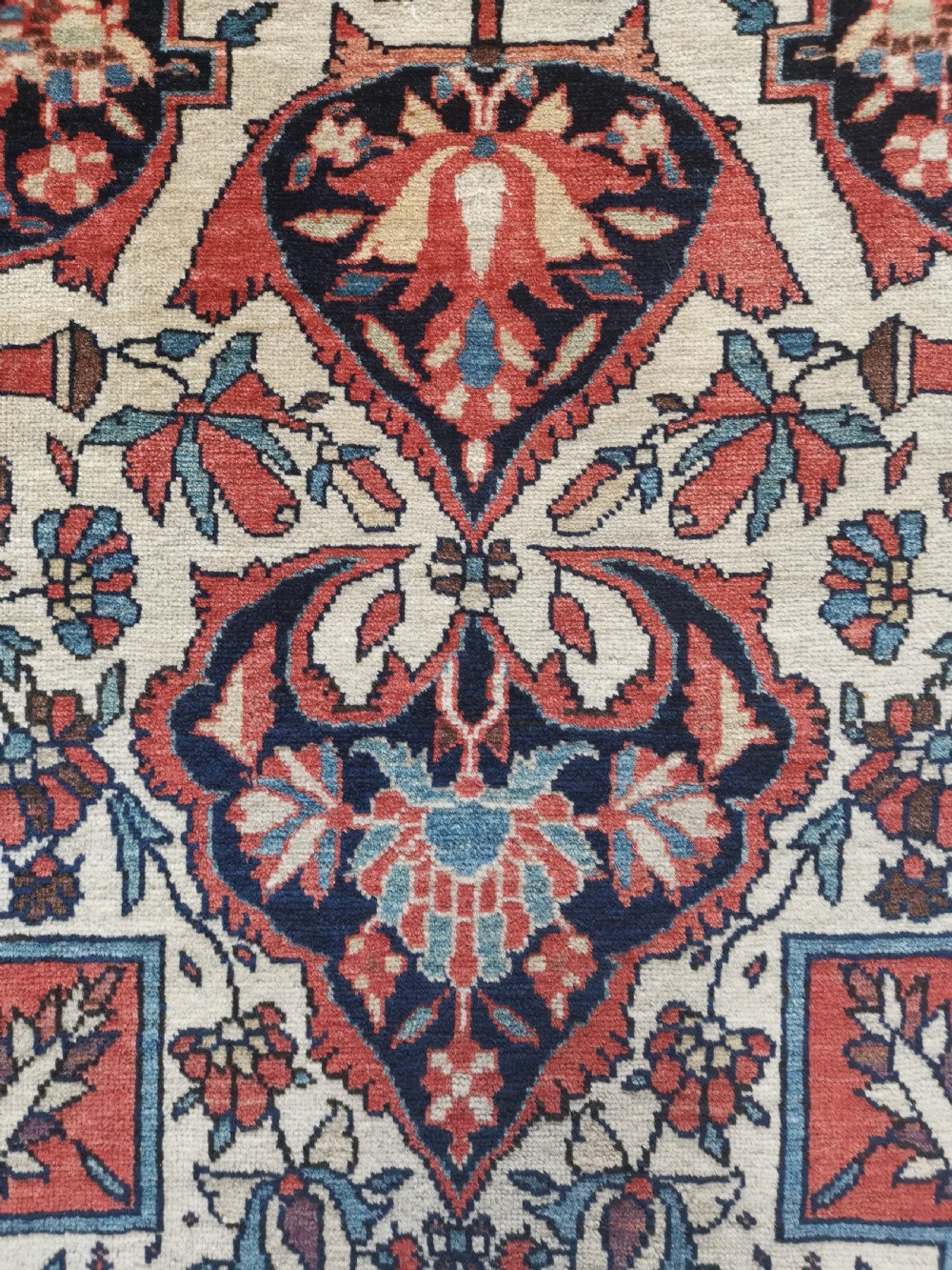 A rectangular hand-knotted antique Persian Sarouk rug featuring a central floral medallion on an ivory field with a navy floral border. View V