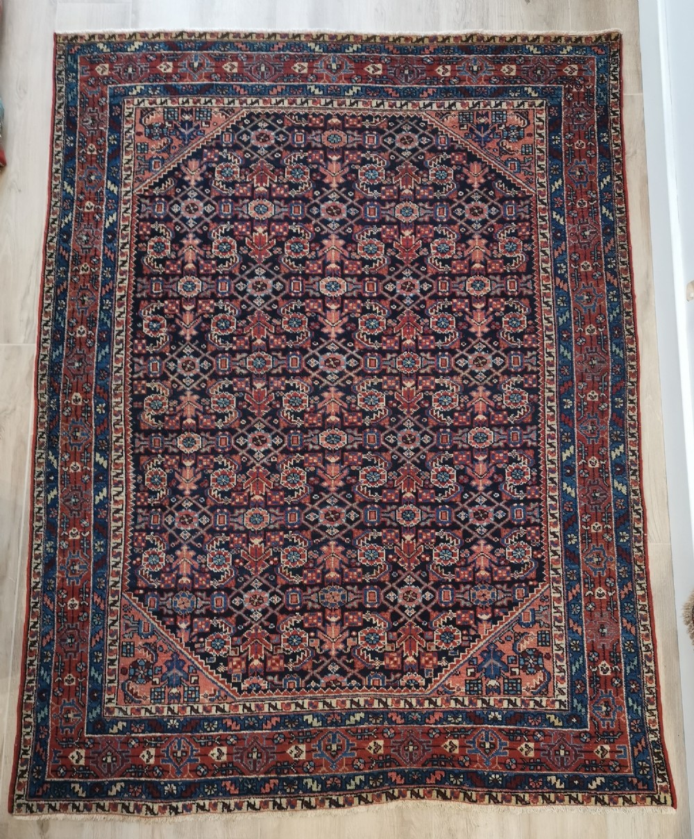 A hand-knotted antique Persian Hamadan wool rug featuring a navy blue field with geometric repeats framed by a terracotta spandrel and detailed multi-band border.
